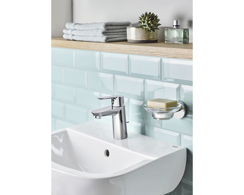 Chiuvetă de baie cu robinet, savonieră, prosoape și accesorii pe un raft