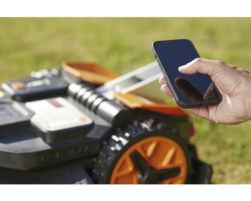 Un bărbat operează o mașină de tuns iarba robotizată cu un smartphone.