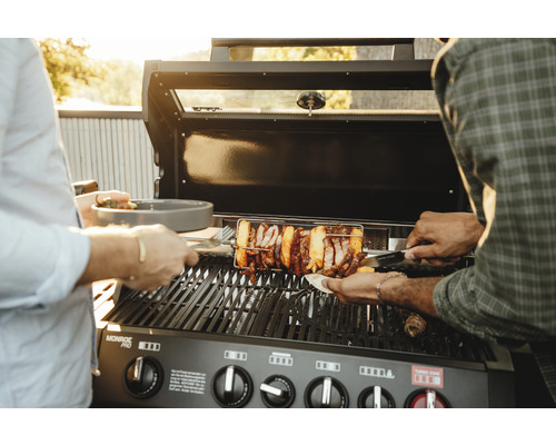 Grătar pe gaz cu rotisor și persoane care grătar mâncare.