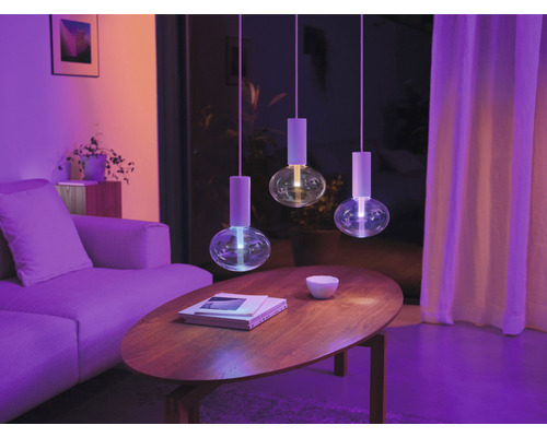 Living cu trei corpuri de iluminat suspendate rotunde deasupra unei mese din lemn