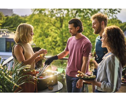 Grup de prieteni care fac grătar pe balcon cu un grătar de masă și se bucură de timp.