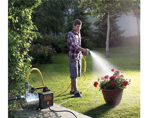 Scenă de grădină cu un bărbat care udă flori cu o pompă de grădină. Logo Black und Decker.