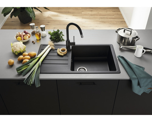 Chiuvetă neagră din granit cu picurător și robinet pe un blat de bucătărie cu legume