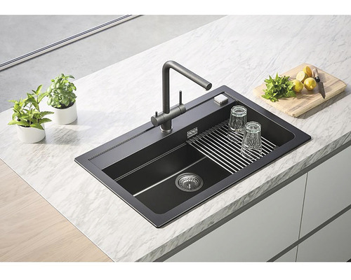 Chiuvetă de bucătărie neagră cu suport pentru scurgere, baterie și accesorii pe un blat de bucătărie.