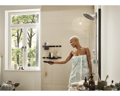 Baie luminoasă cu duș, fereastră și femeie care curăță un perete de duș din sticlă cu o racletă