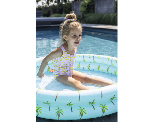 Fetiță se joacă într-o piscină gonflabilă pentru copii cu model de palmieri