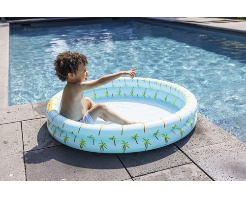 Copil așezat într-o piscină gonflabilă cu model de palmieri