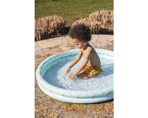Copil se joacă într-o piscină gonflabilă cu model de palmieri în grădină