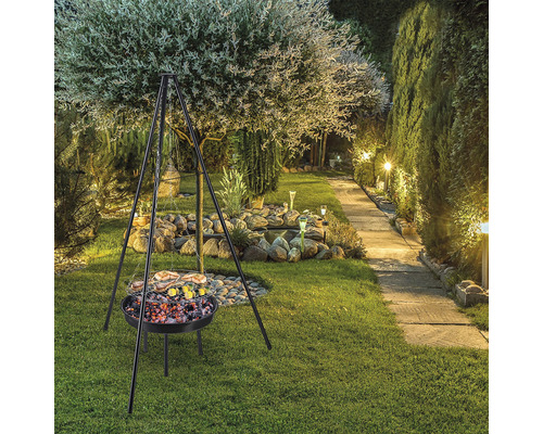 Grătar cu trepied în grădină cu copaci, pietre și gazon