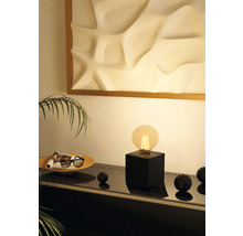 Scenă cu lampă pe soclu negru, bol cu reviste și bile decorative pe o comodă