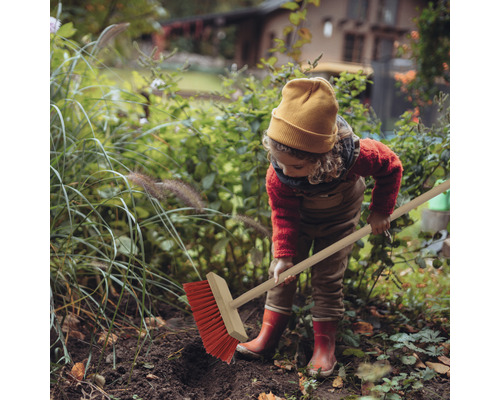 Un copil mătură frunze în grădină cu o mătură de stradă.