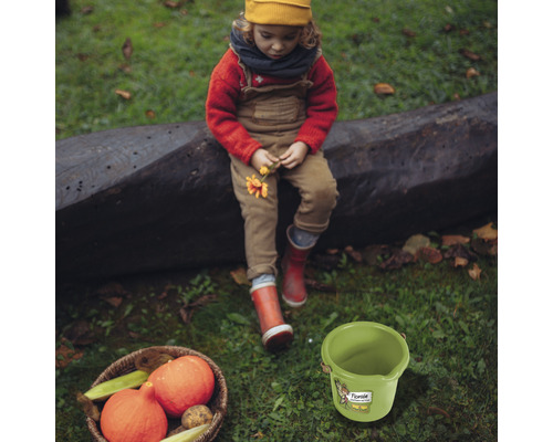 Scenă cu copil, dovleci într-un coș și o găleată verde pe un gazon