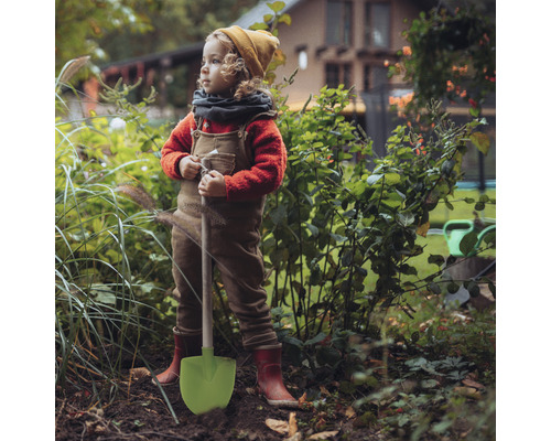 Un copil cu o lopată stă în grădină.