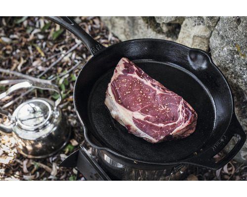 O friptură crudă într-o tigaie de fontă pe un aragaz cu un ceainic lângă