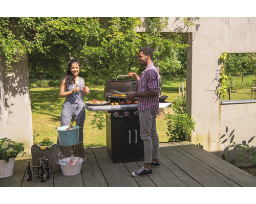 Scenă în aer liber cu un cuplu care face grătar pe un grătar cu gaz în grădina lor.