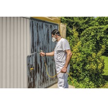 Bărbat vopsește ușa de garaj cu un pulverizator de vopsea. Bricolaj în grădină.