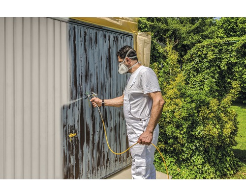 Bărbat vopsește ușa de garaj cu un pulverizator de vopsea. Bricolaj în grădină.