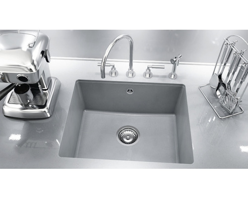 Chiuvetă cu robinet, dozator de săpun, ustensile de bucătărie și aparat de espresso pe un blat.