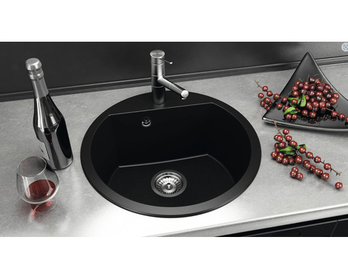 Chiuvetă rotundă din material negru cu robinet și accesorii pe un blat de lucru.