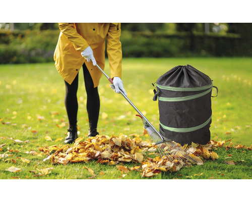 Femeie adună frunze cu o greblă și un sac de grădină