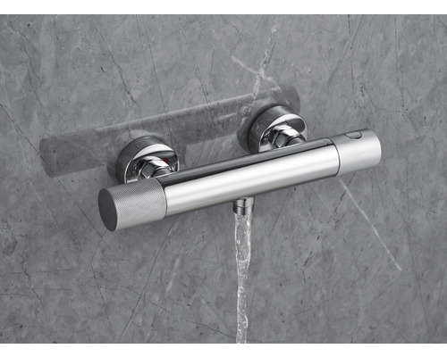 Baterie termostatică aparentă cu flux de apă în fața unui perete gri