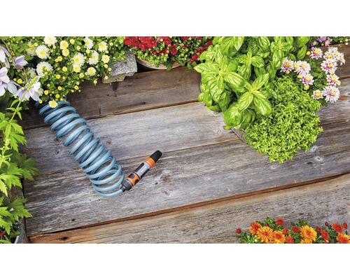 Scenă de grădină cu furtun spiralat, flori și ierburi aromatice pe podea de lemn