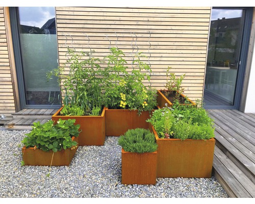 Mai multe jardiniere ruginite de diferite dimensiuni cu plante în grădină.