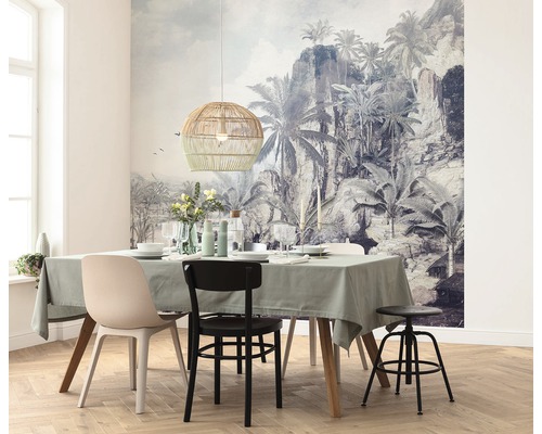 Sufragerie cu masă, scaune, lampă suspendată din ratan și fototapet tropical.