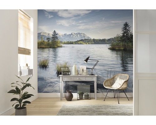 Cameră de zi cu tapet de perete care prezintă un lac și munți, plus o masă, o lampă și un scaun.