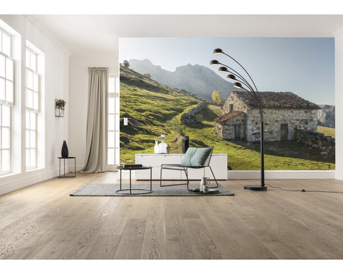 Cameră de zi cu fototapet cu o casă de piatră într-un peisaj verde colinar