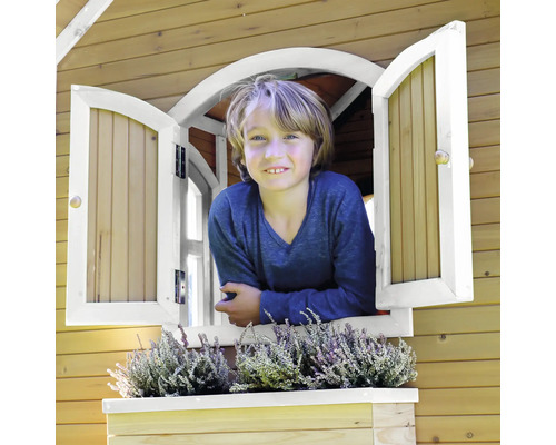 Băiat care se uită pe fereastra unei căsuțe de joacă din lemn cu jardinieră