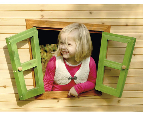 O fetiță blondă se uită pe fereastra unei căsuțe de joacă din lemn.