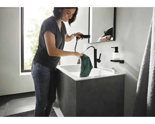 Femeie spălând o cârpă într-un lavoar cu robinet negru și duș de mână într-o baie modernă