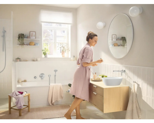 Baie luminoasă cu oglindă ovală, chiuvetă și cadă.