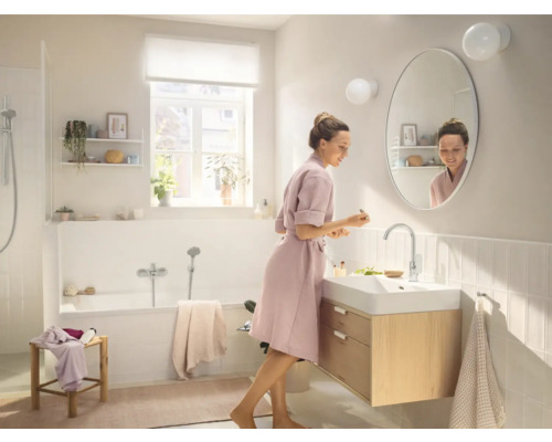 Baie luminoasă cu cadă, dulap sub chiuvetă și femeie în fața oglinzii