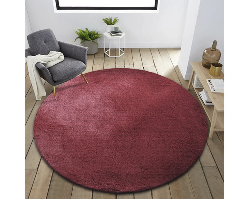 Interior cu covor rotund, vișiniu, fotoliu, măsuță laterală și raft din lemn