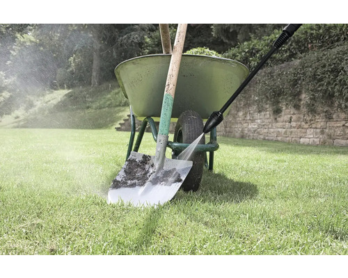 Curățător cu înaltă presiune curățând cazmaua în fața roabei în grădină