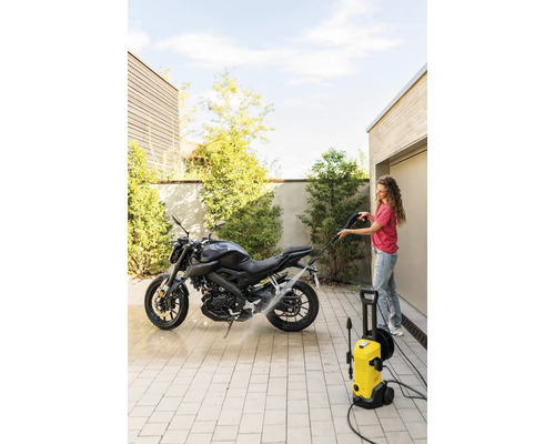 Femeie curăță motocicletă cu un aparat de curățat cu presiune afară.