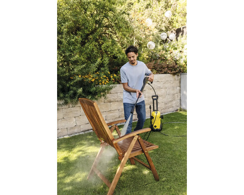 Un bărbat curăță un scaun de lemn în grădină cu un aparat de curățat cu presiune.