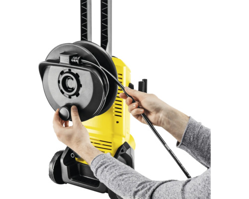 Persoană înfășurând furtunul pe un aparat de curățat cu presiune galben