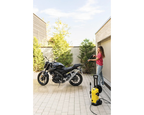 Femeie care curăță o motocicletă cu un aparat de spălat cu presiune galben în aer liber