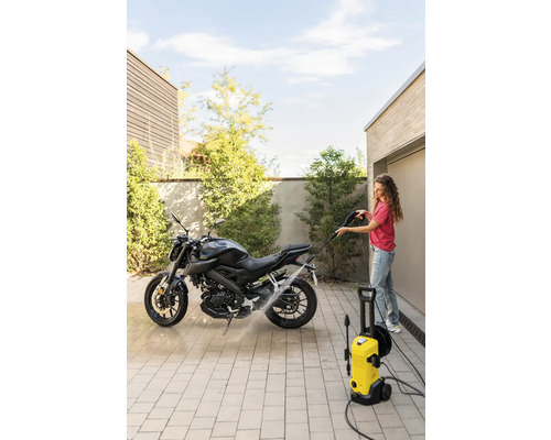 Femeie care curăță o motocicletă cu un curățător cu presiune într-o curte pavată.