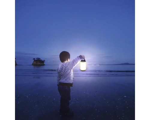 Un copil stă pe plajă și ține un felinar.