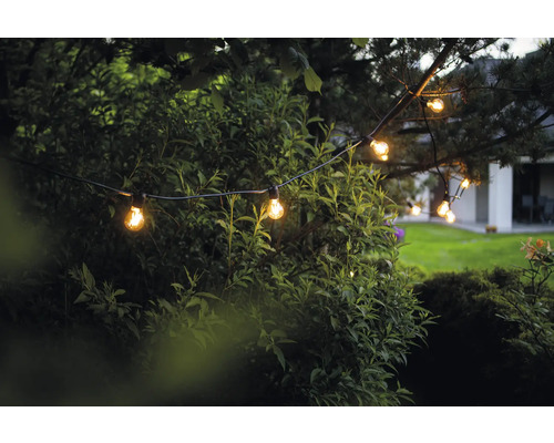 Șirag luminos cu becuri în grădină printre copaci și arbuști