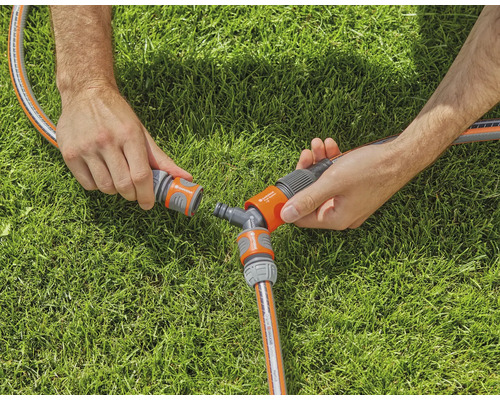 Două mâini conectează un furtun de grădină la un racord în Y pe un gazon.