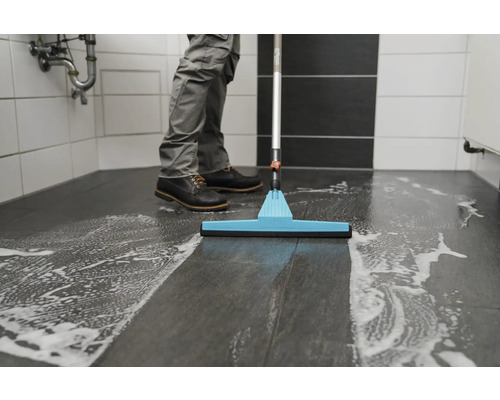 Agent de curățare șterge podeaua băii cu detergent și racletă