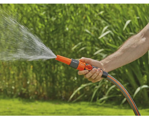 O persoană ține un furtun de grădină cu duză de pulverizare, din care curge apă.