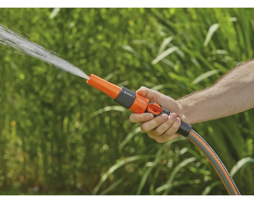 O mână ține un duș de grădină din care țâșnește apă.