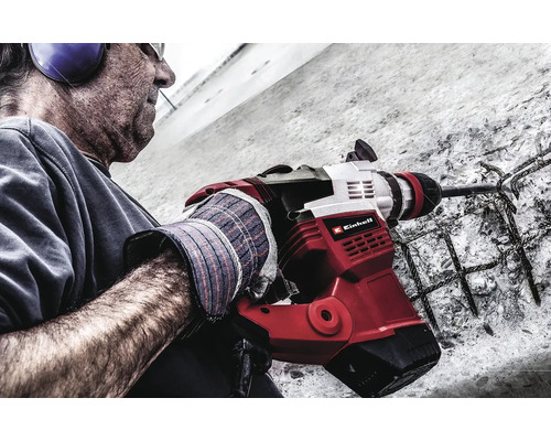 Un bărbat folosește un ciocan demolator Einhell pe un perete de beton cu armătură de oțel. Logo-ul Einhell este vizibil.
