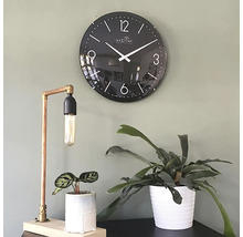 Scenă decorativă cu un ceas de perete negru, o lampă de masă din cupru și două plante de interior în ghivece.